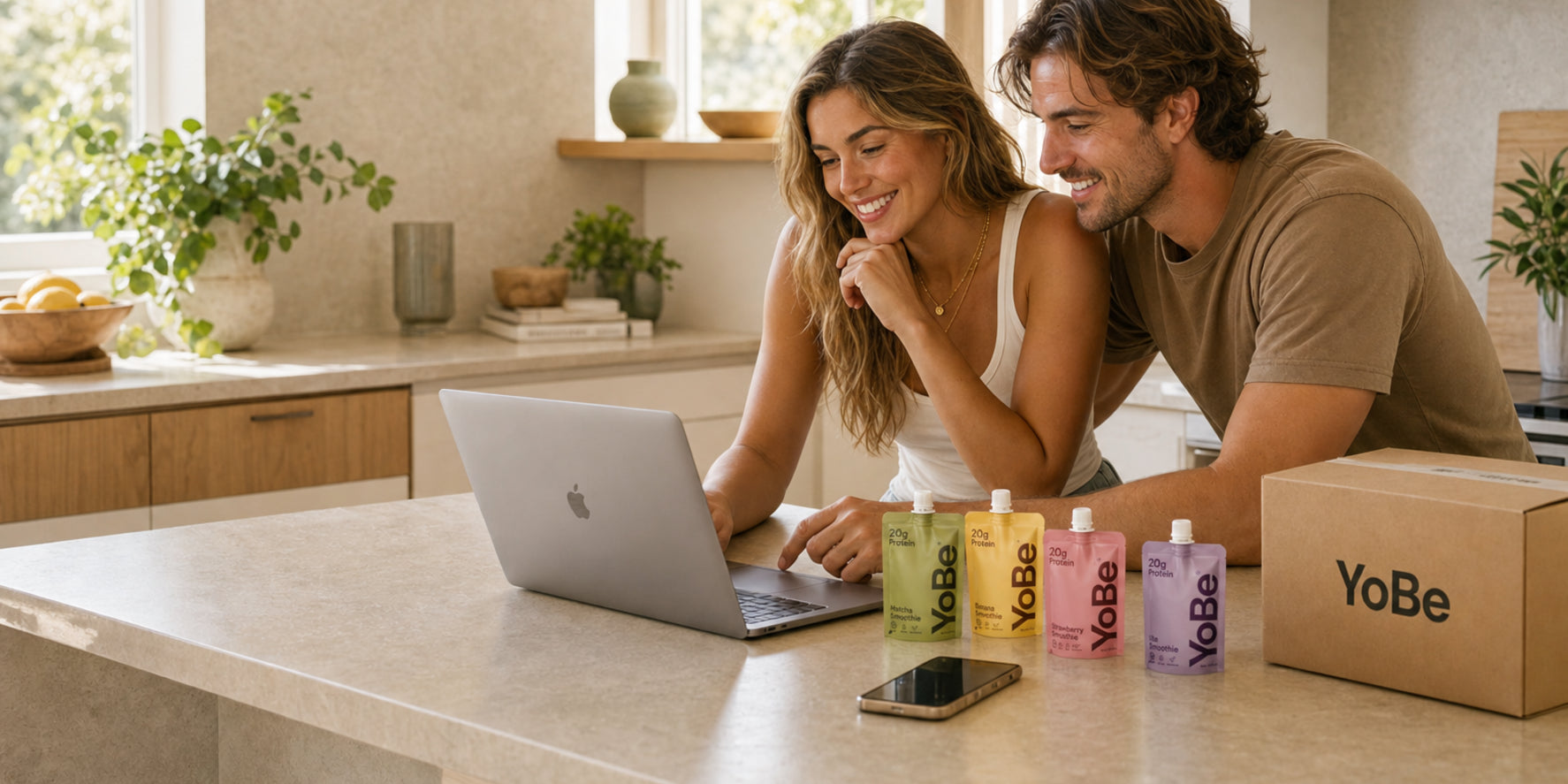 Couple ordering more YoBe on a laptop in a bright kitchen with pouches and a delivery pack on the counter